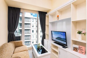 A modern living room with a sofa, a coffee table, a TV, and a view of a building through the window. - Comfortable And Homey 1Br At Apartment Tree Park City Bsd (Tangerang)