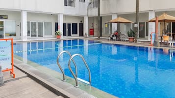 A swimming pool with clear blue water, surrounded by a tiled deck. There are lounge chairs and umbrellas, and a sign indicating the pool's depth.
