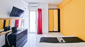 Quarto de hotel com cama, escrivaninha com computador, televisão, espelho e porta de correr para uma varanda.