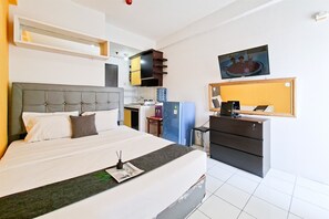 Habitació d'hotel amb llit, escriptori, prestatge, televisió i dispensador d'aigua.