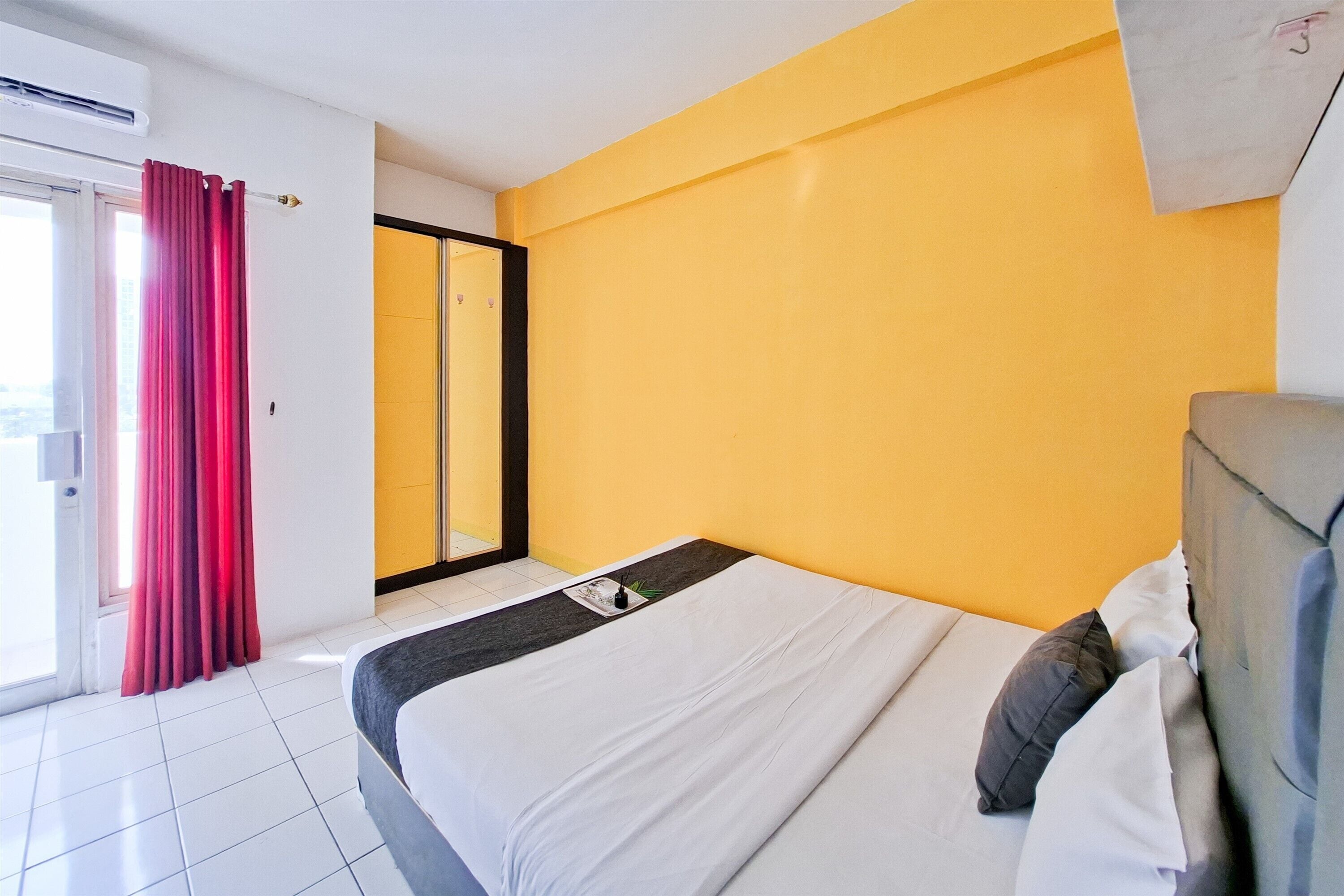 A hotel room with a bed, a window with curtains, and a yellow wall.