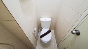 Casa de banho pequena e estreita, com sanita, secador de mãos e porta com puxador redondo.