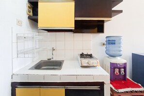Una cocina con un lavamanos, una estufa a gas, un dispensador de agua y un estante con una botella de agua.