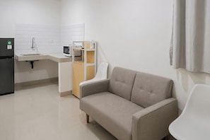 A kitchenette with a refrigerator, microwave, sink, and cabinet. There is a beige sofa and a white chair in the living area. - Serene Modern 1Br (No Kitchen) At Apartment Bandaraya - Tallasa City Makassar (Makassar (Ujung Pandang))