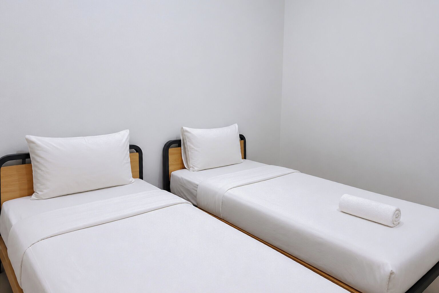 Dos llits individuals amb els capçals de fusta i roba de llit blanca en una habitació amb parets sense decoració.
