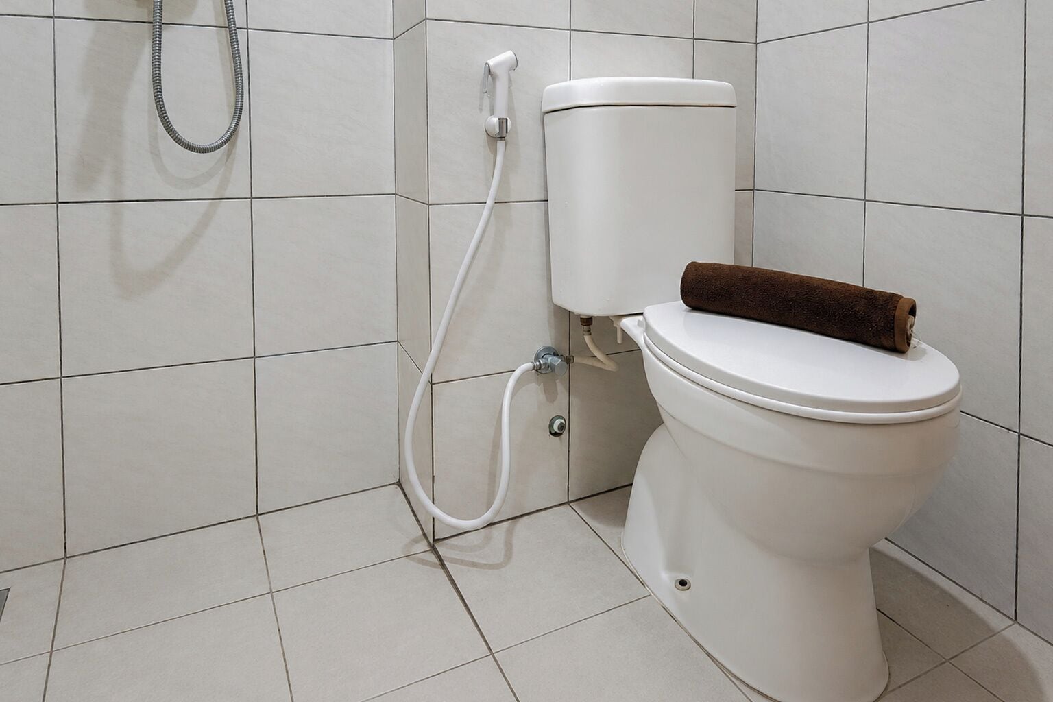 A white toilet with a brown towel on top, a white tank, and a shower hose.