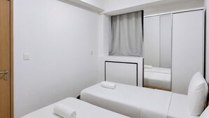 Habitació d'hotel amb dos llits individuals, una porta de fusta, un mirall i una finestra amb cortina.