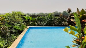 A rectangular pool surrounded by lush greenery and a wooden fence. - Bright And Comfortable Studio Room At Apartment Tuscany Residence (South Tangerang)