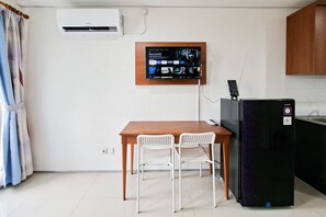 A small kitchenette with a refrigerator, a wooden table with two chairs, and a wall-mounted TV. - Bright And Comfortable Studio Room At Apartment Tuscany Residence (South Tangerang)