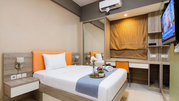 A modern hotel room with a bed, bedside table, desk, and a television. - Calming Wooden Touch Studio Room At Apartment Soekarno Hatta (Suhat) Malang (Malang)