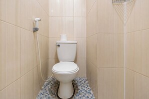 A small, tiled bathroom with a toilet, a shower, and a toilet paper holder.