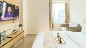 Una habitación de hotel con cama, televisor montado en la pared, ventana con cortinas y una mesita con bandeja.