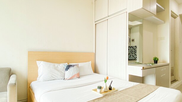 A hotel room with a bed, a bedside table, a chair, and a mirror. - Minimalist Functional Studio At Apartment Grand Kamala Lagoon (Bekasi)