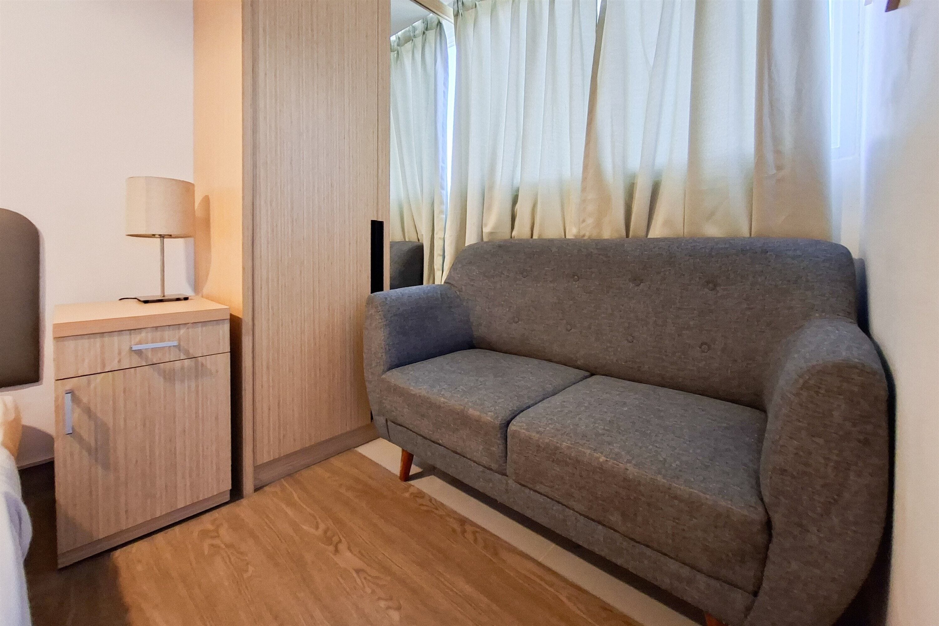 A small room with a grey sofa, a wooden cabinet, and a lamp.