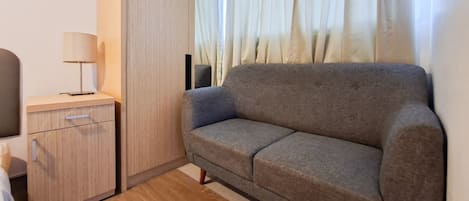 Et lille rum med en grå sofa, et træskab og en lampe.