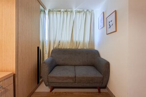 Ein Zimmer mit einem grauen Sofa, einem Holzschrank und einem Fenster mit Vorhängen.