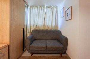 Quarto com sofá cinza, um armário de madeira e uma janela com cortinas.