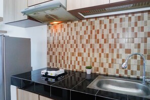 A kitchen with a black countertop, a sink, a stove, and a tiled backsplash. - Decent And Homey Studio Room At Apartment Margonda Residence 5 (Depok)