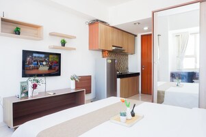 Una habitación de hotel moderna con televisión de pantalla plana, un escritorio de madera, una cama y una kitchenette.
