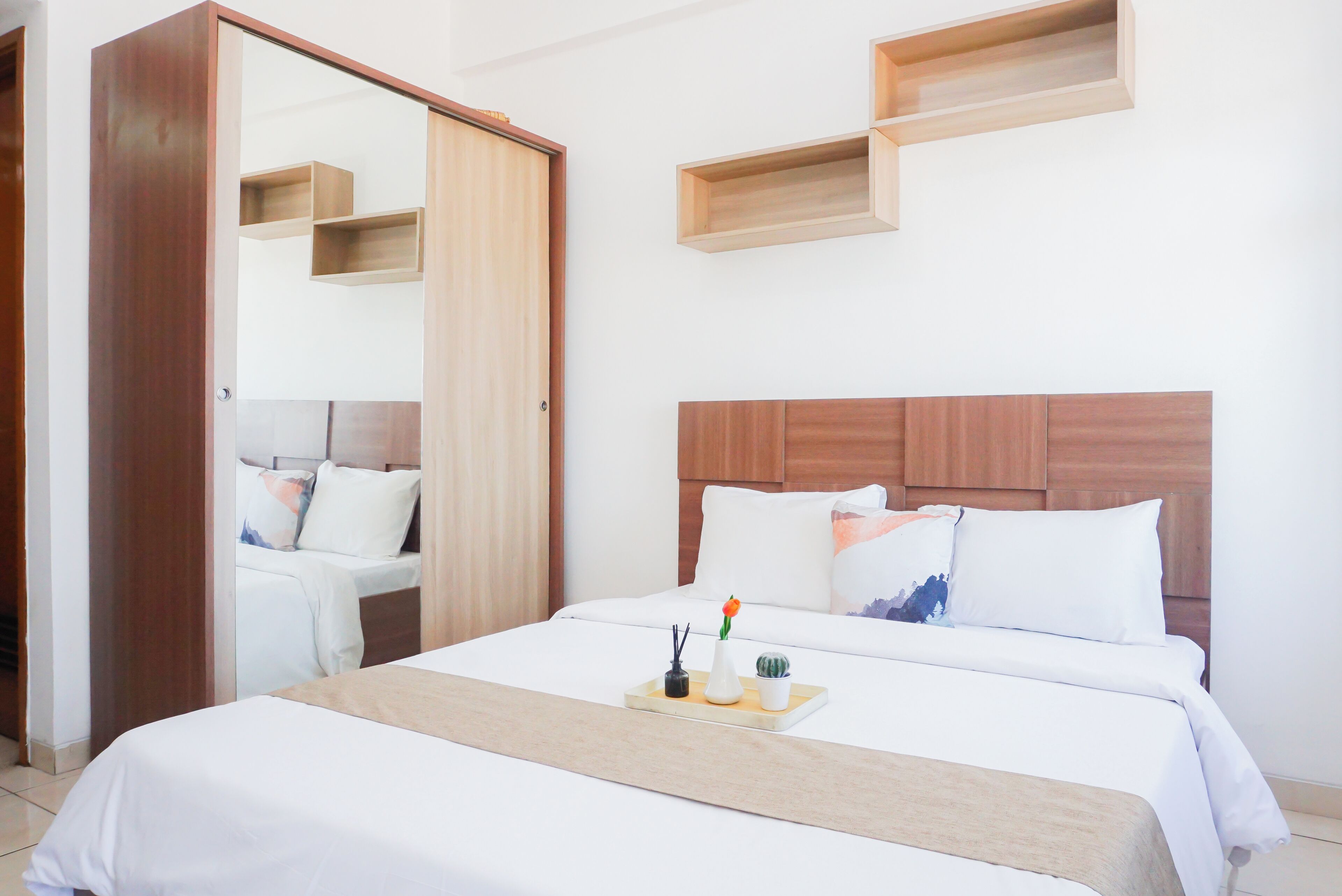 A hotel room with a bed, bedside tables, a wardrobe, and built-in shelves.