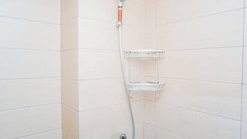 A shower with a handheld showerhead and a wall-mounted shelf.
