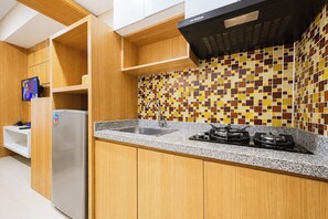A kitchen with wooden cabinets, a tiled backsplash, a stainless steel sink, and a gas stove. - Comfortable And Practical Living Studio Room At Apartment Tamansari Papilio (Surabaya)