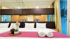 A hotel room with a bed, a bedside table with a vase and plants, and a television in the background. - Comfortable And Practical Living Studio Room At Apartment Tamansari Papilio (Surabaya)