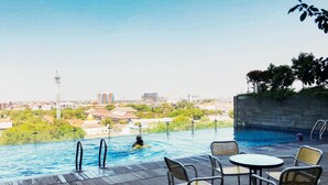 An outdoor swimming pool with a city view, surrounded by lounge chairs and tables. - Comfortable And Practical Living Studio Room At Apartment Tamansari Papilio (Surabaya)