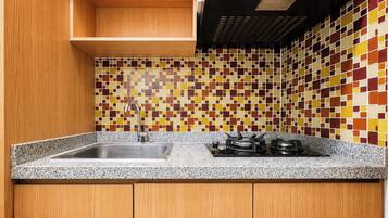 A kitchen with a granite countertop, a stainless steel sink, a gas stove, and a tiled backsplash with a geometric pattern.