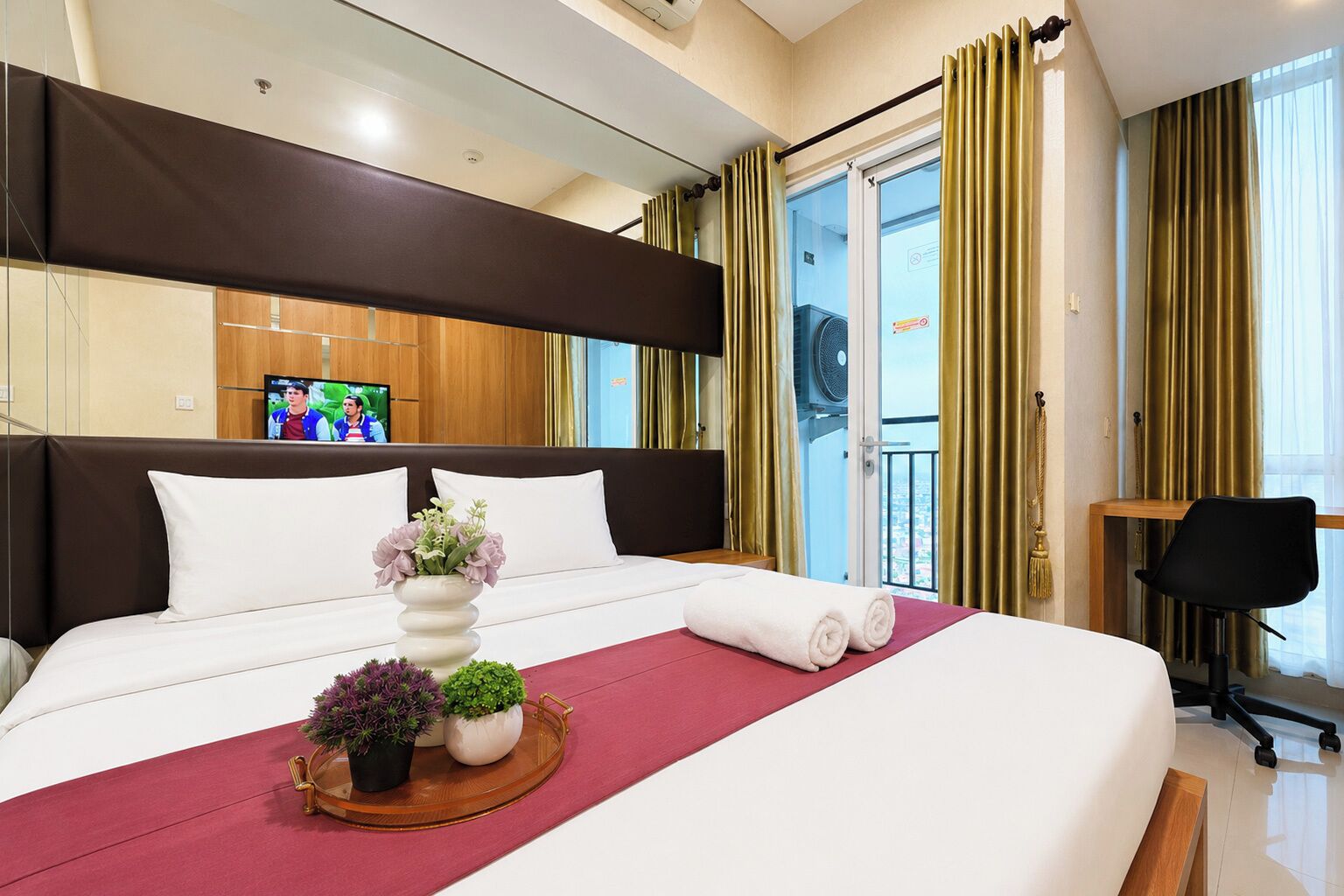 Une chambre d’hôtel avec un grand lit, une télévision, un balcon avec des rideaux et un bureau avec une chaise.