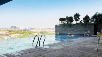 An outdoor infinity pool with a city view, a wooden deck, and a stone wall with greenery.