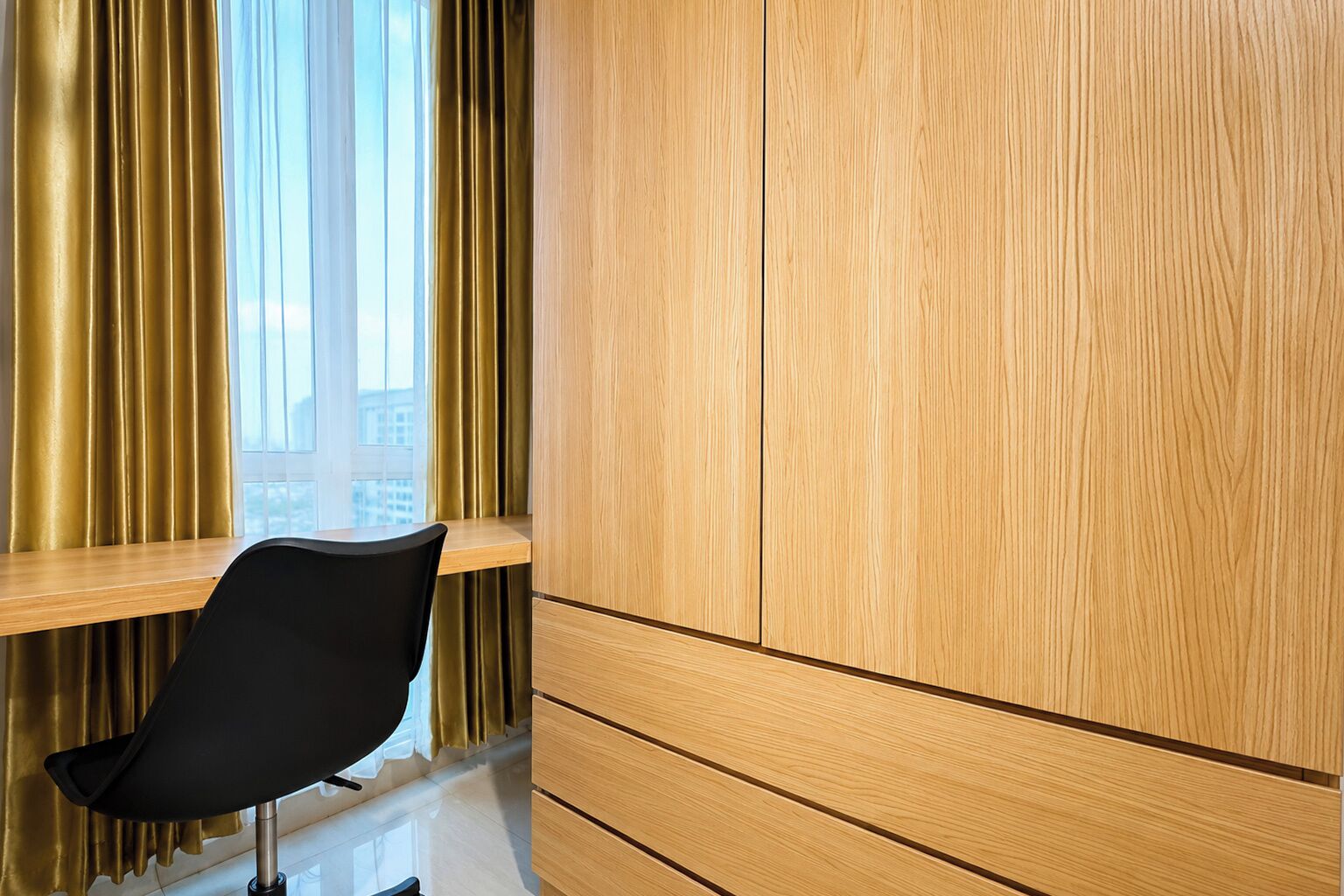 Una habitación con un armario de madera, una silla negra y una ventana con cortinas.