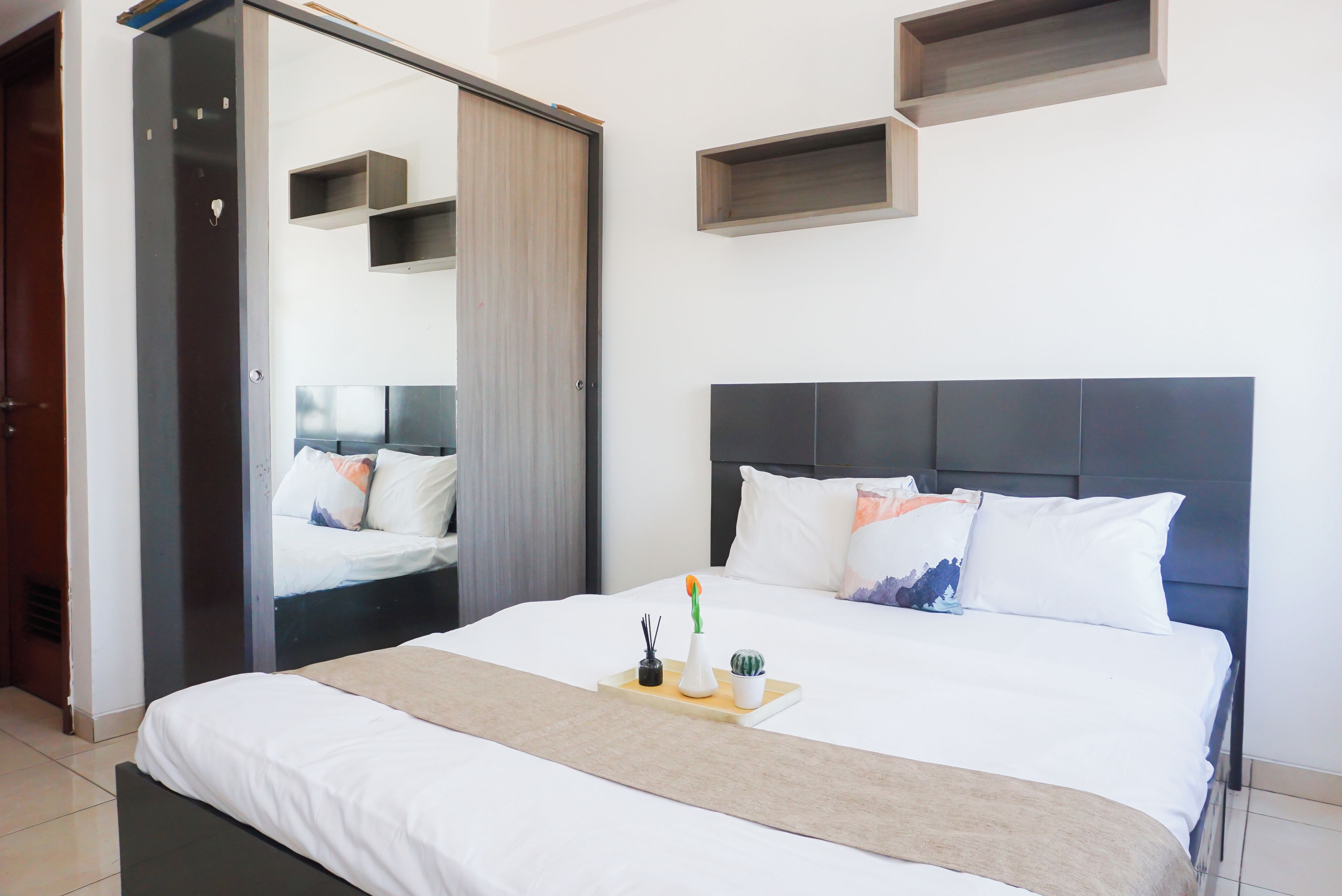 A modern bedroom with a large bed, a bedside table with a tray, a mirror, and built-in shelves.