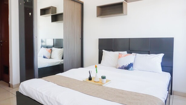 A modern bedroom with a large bed, a bedside table with a tray, a mirror, and built-in shelves. - Cozy And Relaxing Studio At Apartment Margonda Residence 5 (Depok)