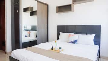A modern bedroom with a large bed, a bedside table with a tray, a mirror, and built-in shelves.