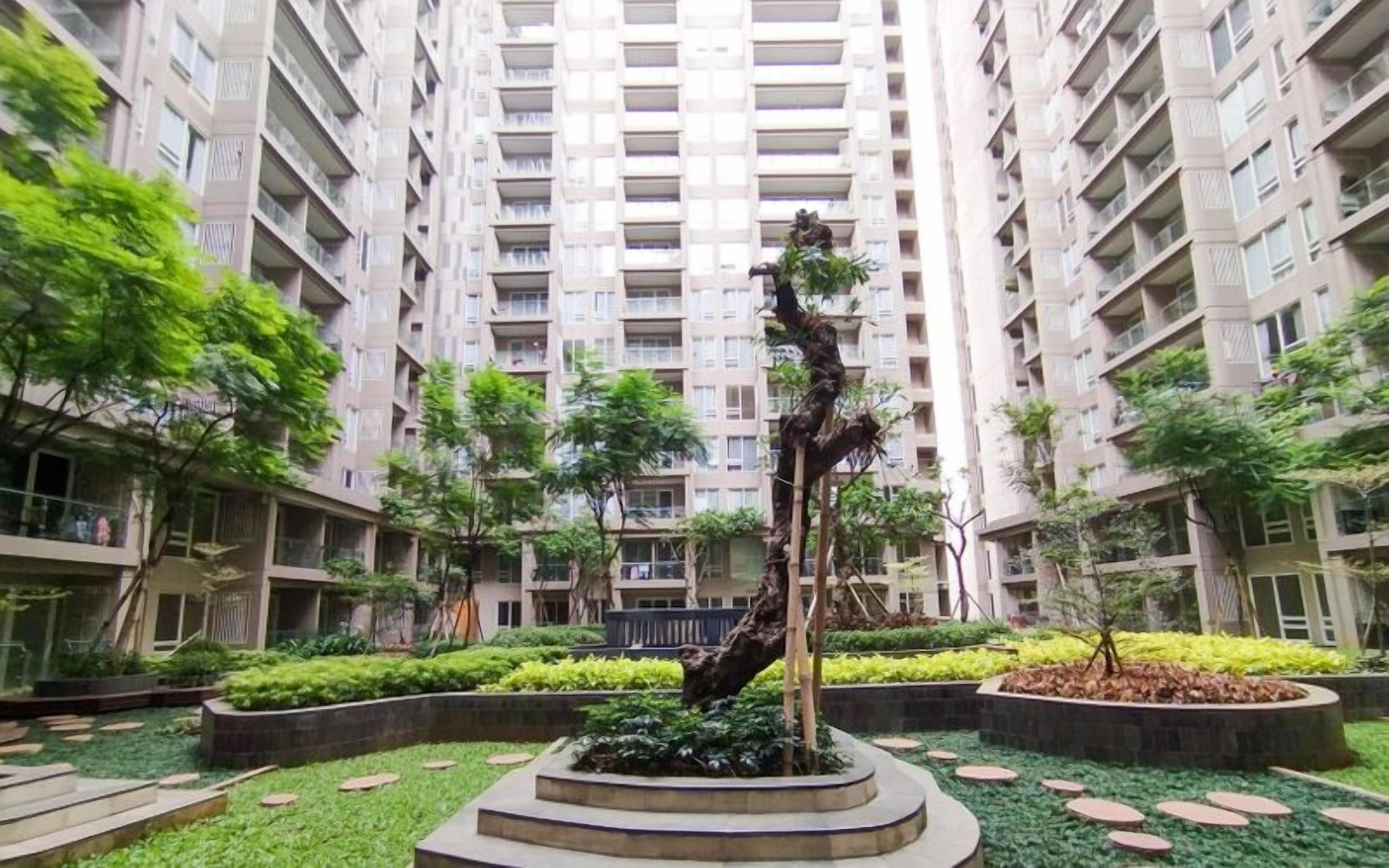 Un patio con una escultura central, rodeado de follaje y un edificio alto al fondo.