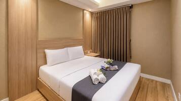 A hotel room with a bed, wooden headboard, curtains, and a small table with a flower arrangement.