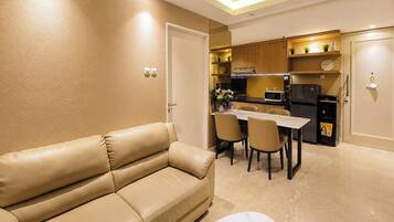 A modern living room with a beige leather sofa, a dining table with chairs, and a kitchen area with wooden cabinets and appliances.