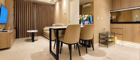 A modern hotel room with a dining area, a TV, and a kitchen.