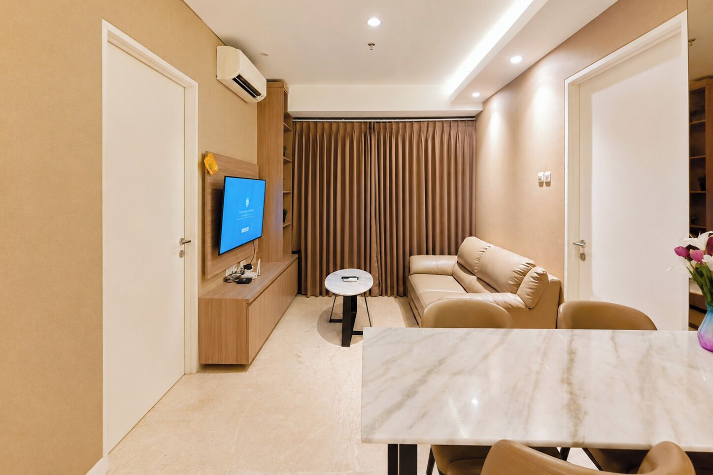 A modern hotel room with a flat-screen TV, a sofa, a small round table, and a marble-topped dining table.