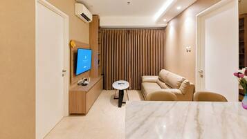 A modern hotel room with a flat-screen TV, a sofa, a small round table, and a marble-topped dining table.