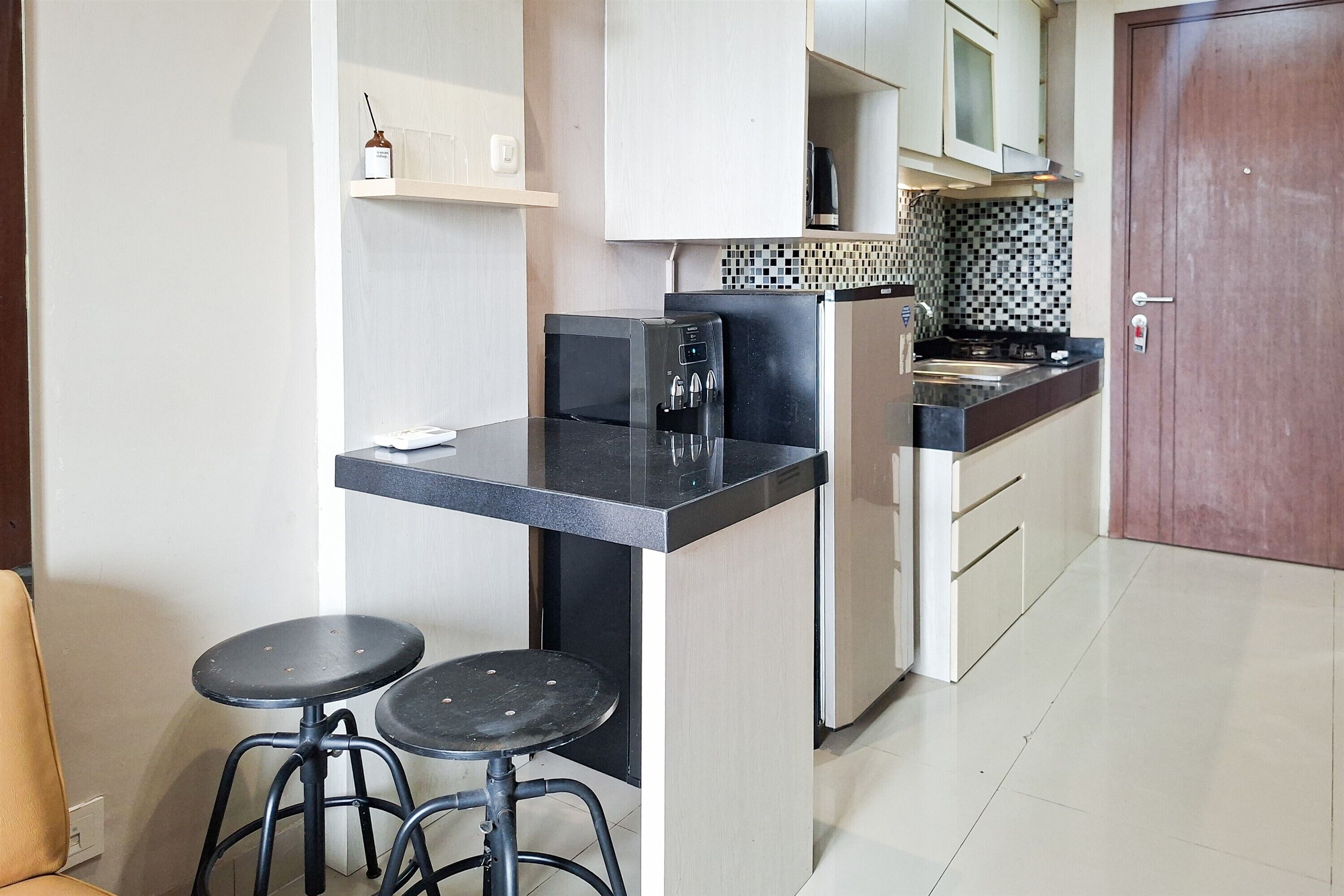 A compact kitchen with a black countertop, a coffee machine, and two stools.