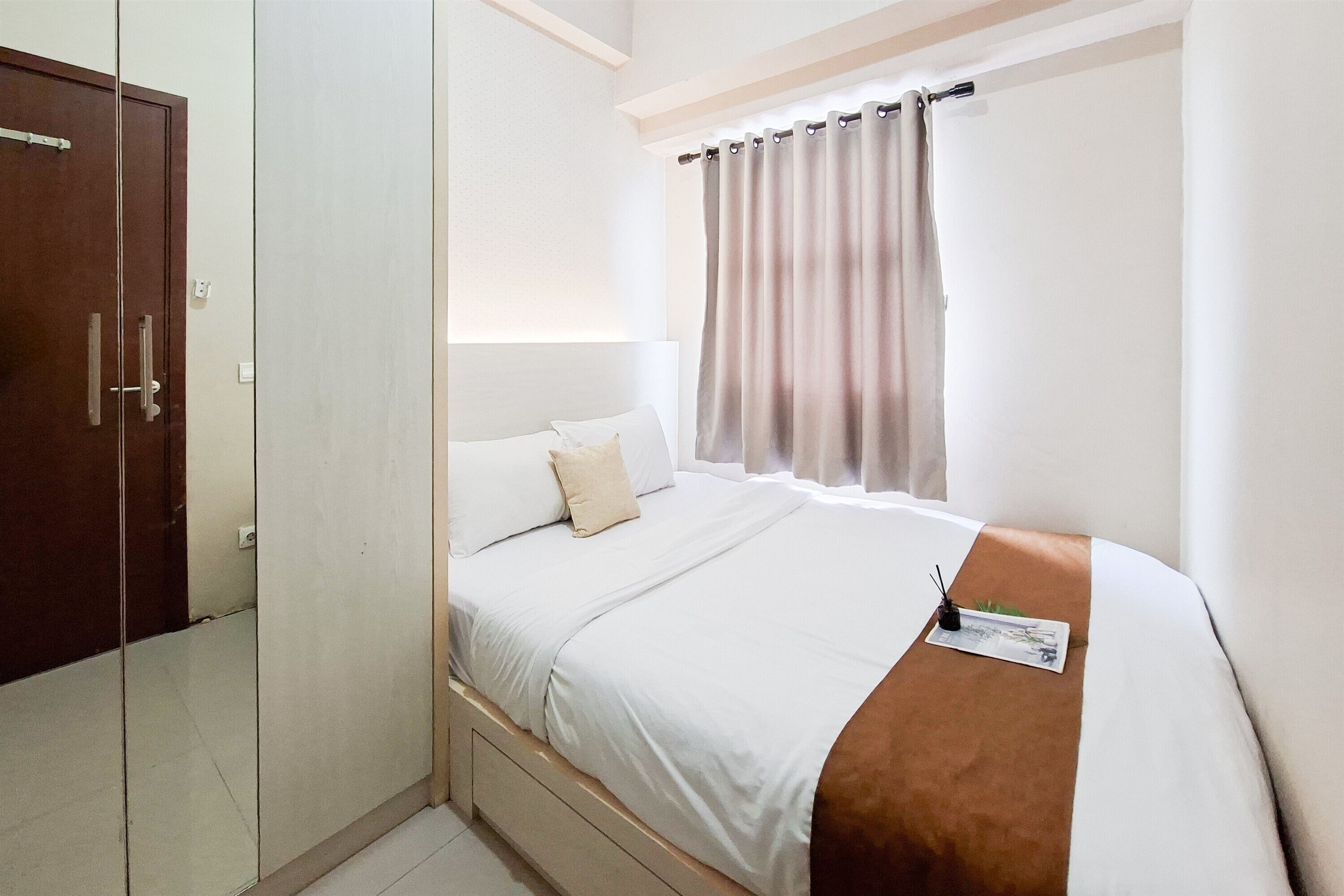 Una habitación de hotel con cama, armario, ventana con cortinas y mesita de noche con lámpara.