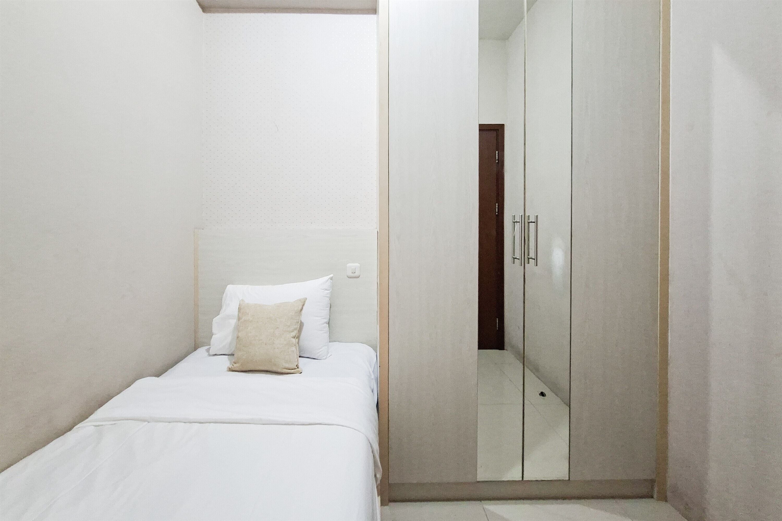 Quarto pequeno com uma cama de solteiro, guarda-roupa e espelho.