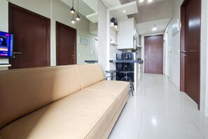 A modern living room with a beige sofa, a kitchen area with a refrigerator and a microwave, and a hallway leading to a door. - Comfortable Modern Look 2Br At Apartment Parkland Avenue (Tangerang)