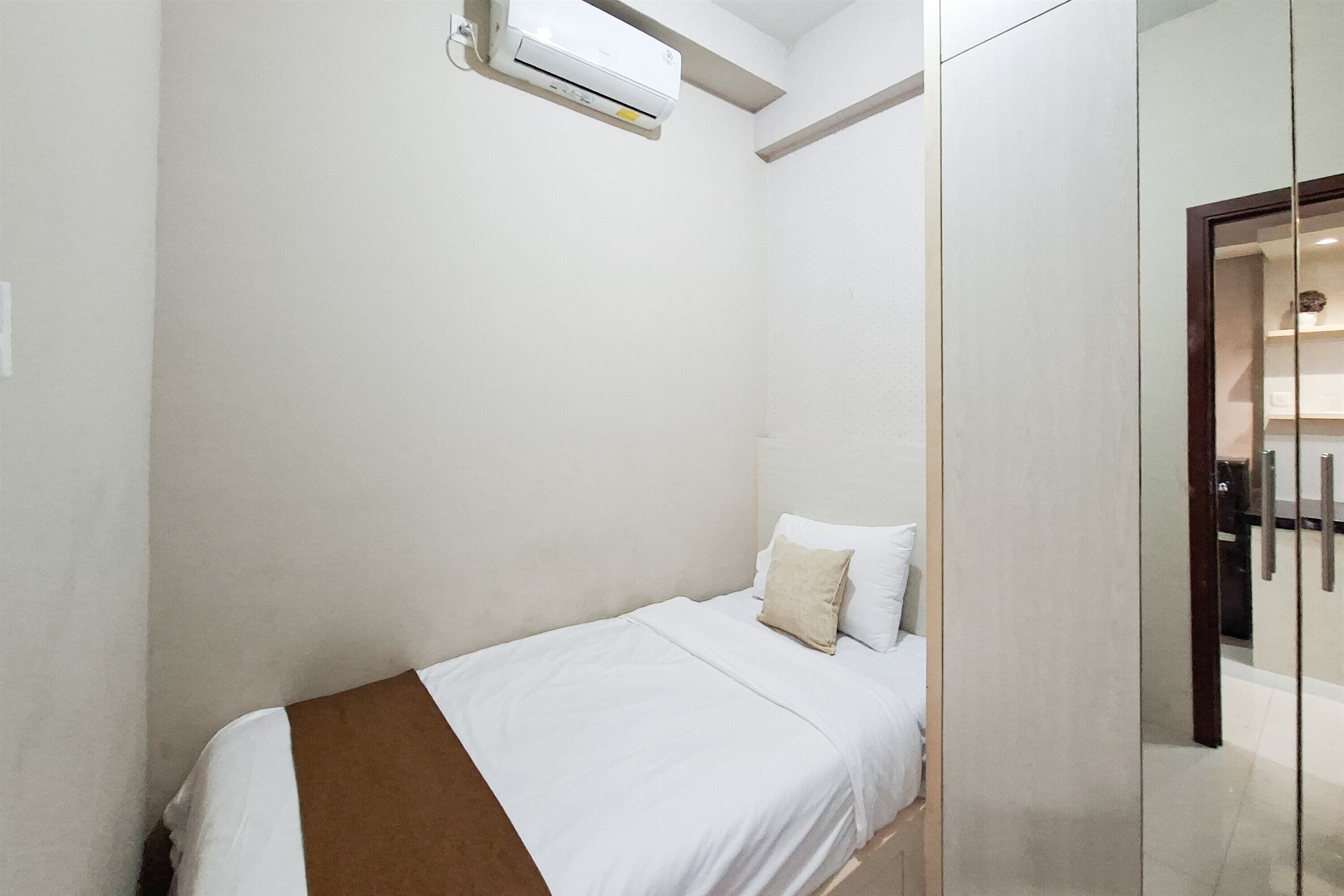 Un lit simple avec une couvre-lit blanche et marron, dans une pièce aux murs blancs et dotée d’une cloison en verre.