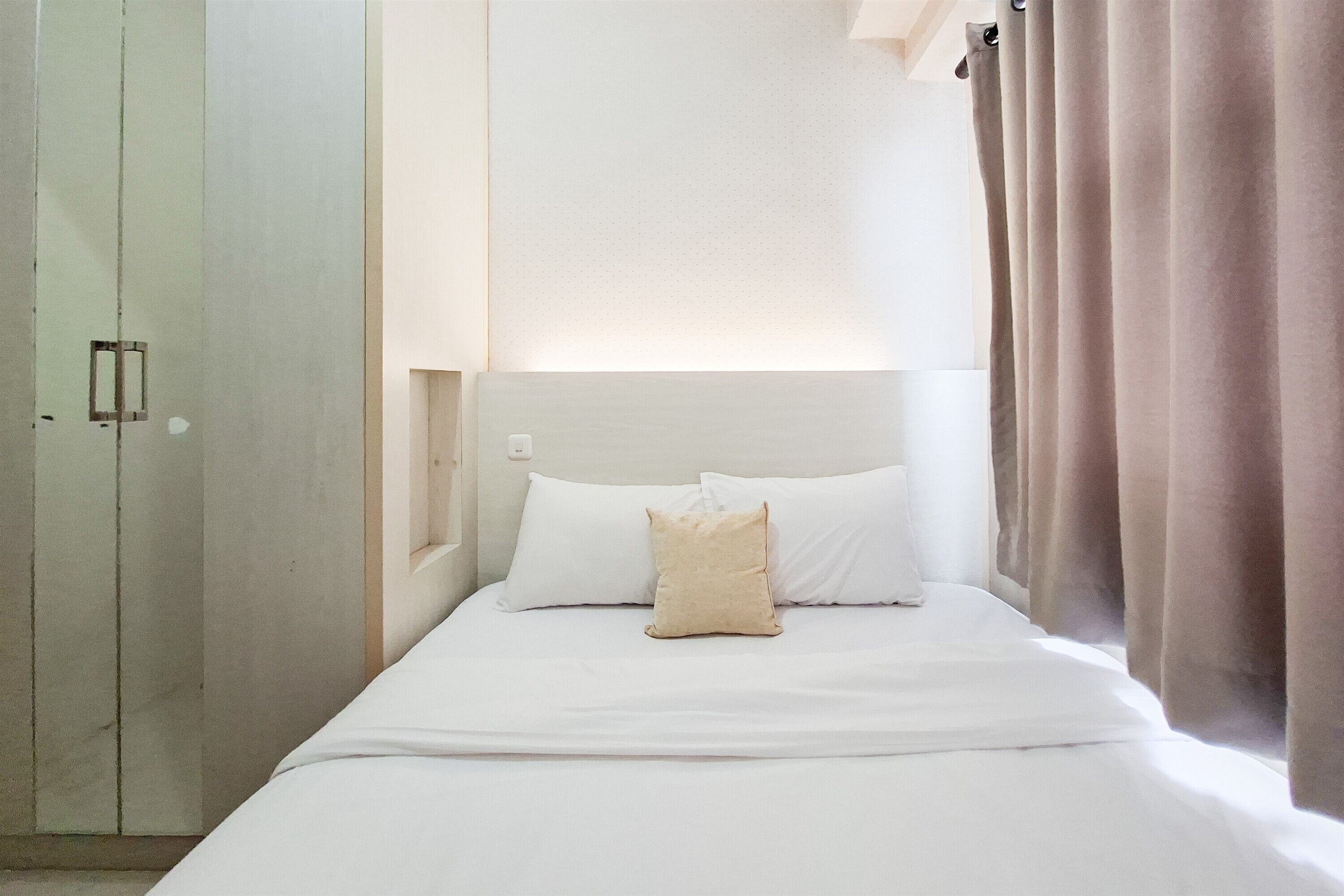 Una habitación de hotel con cama, mesita de noche, armario y ventana con cortinas.