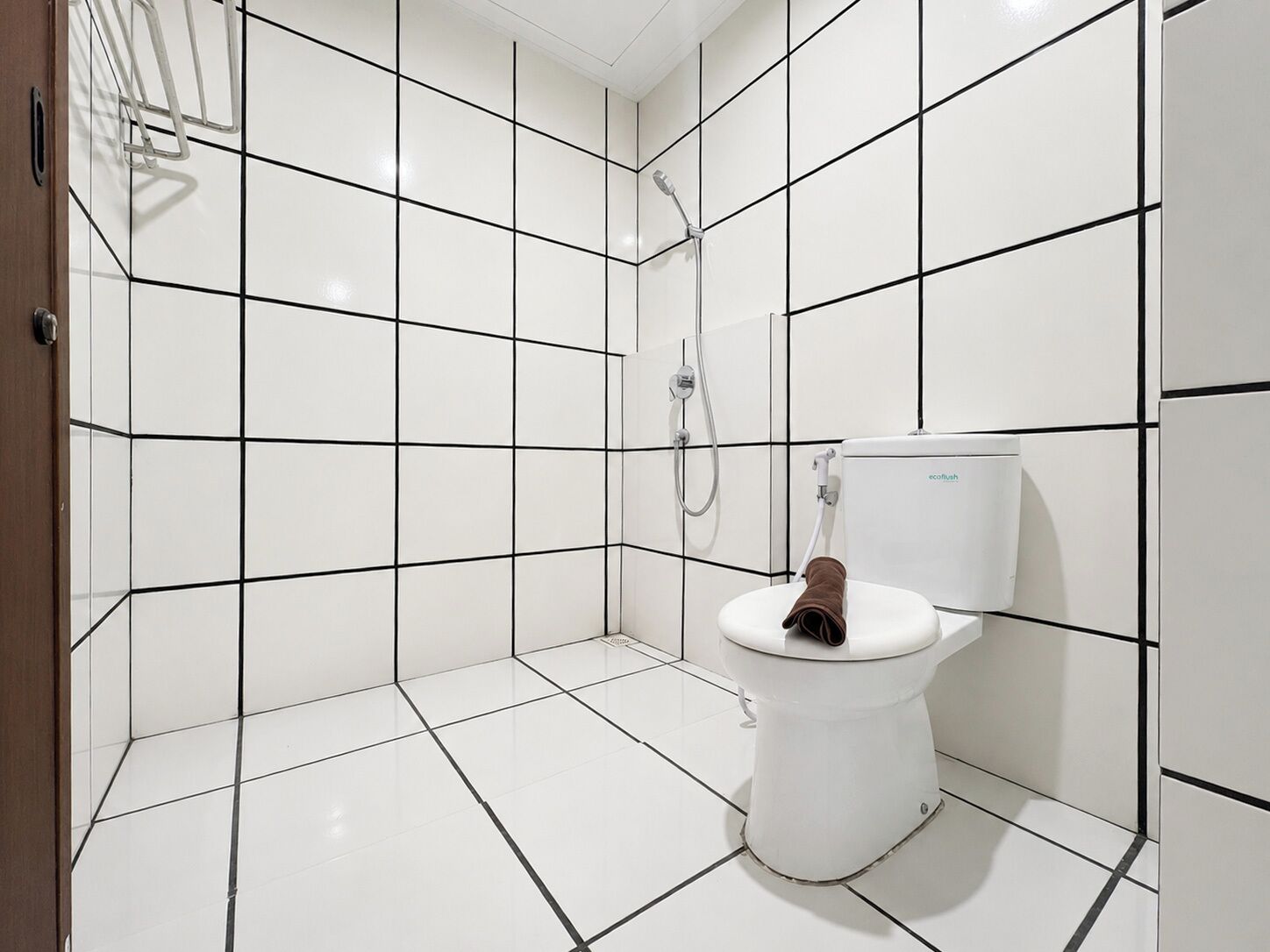 Un baño con paredes y suelo de baldosas blancas, un inodoro blanco y una zona de ducha.