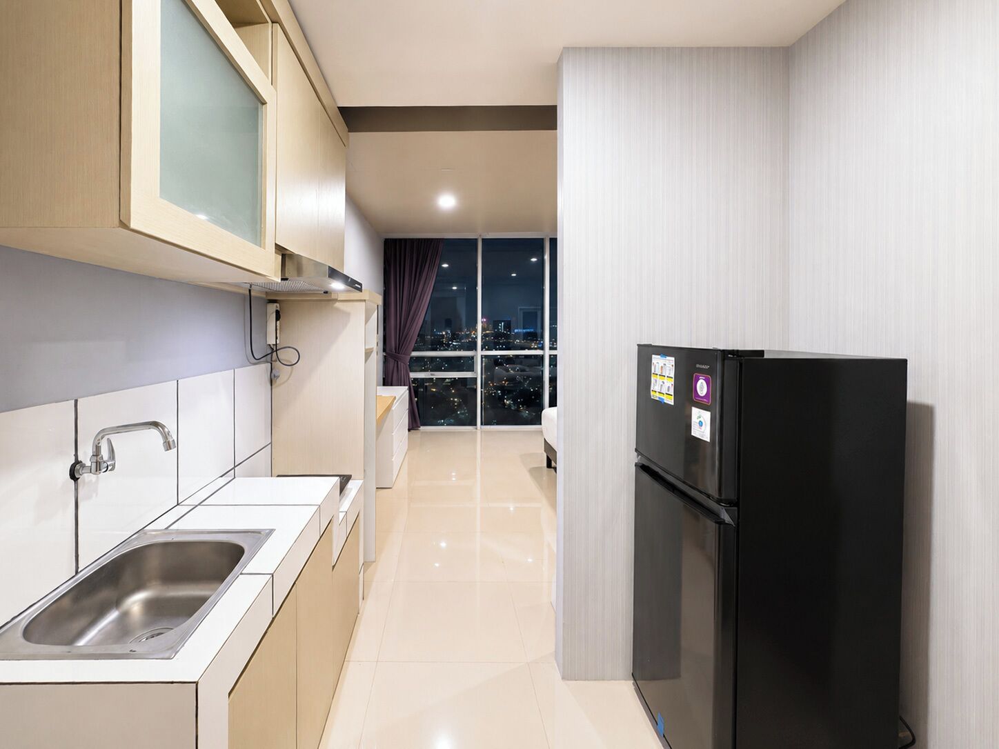 A modern kitchen with a stainless steel sink, a black refrigerator, and a city view through large windows.