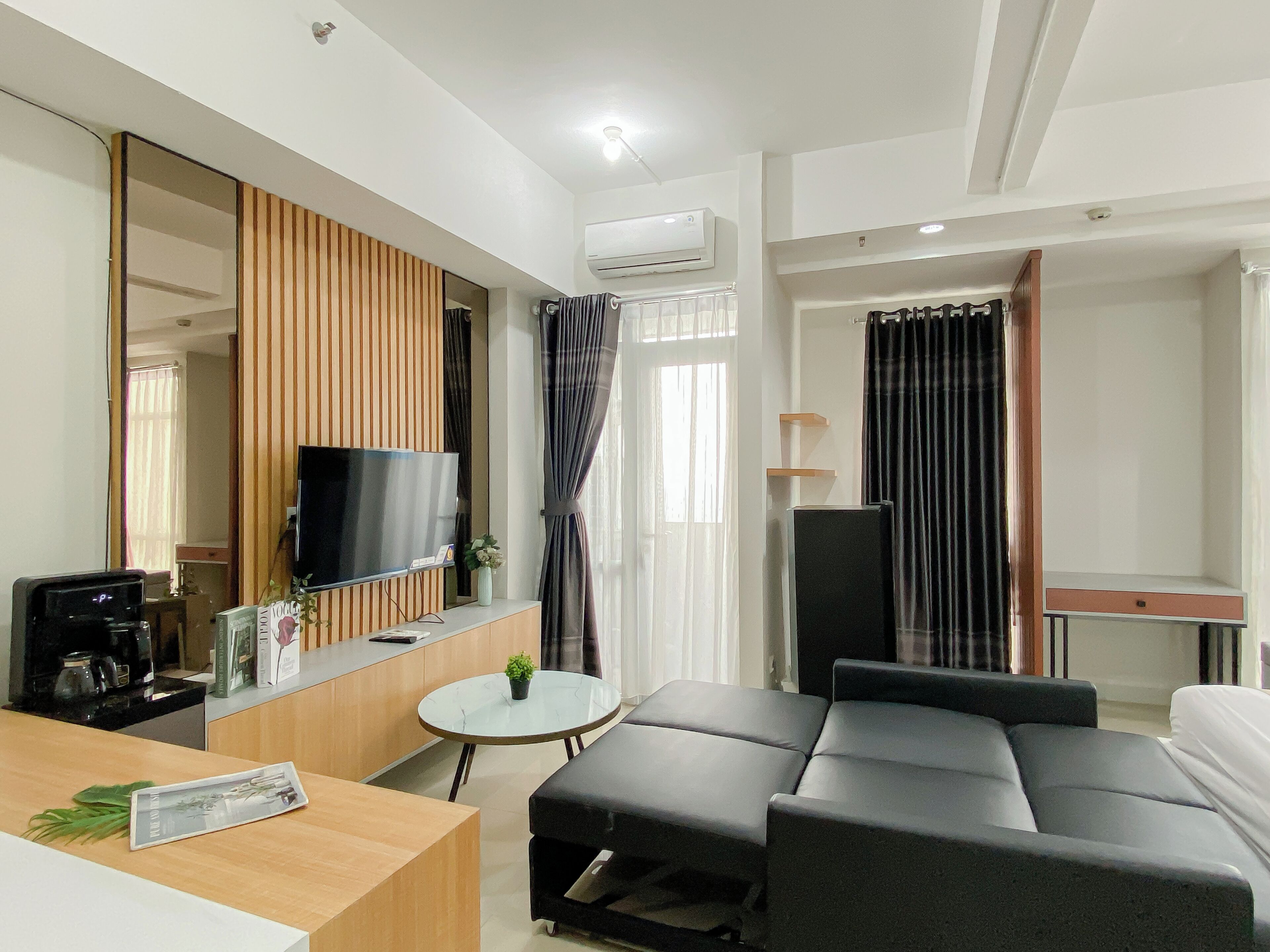 Una habitación de hotel moderna con una televisión de pantalla plana, un sofá, una pequeña mesa redonda y una cafetera.